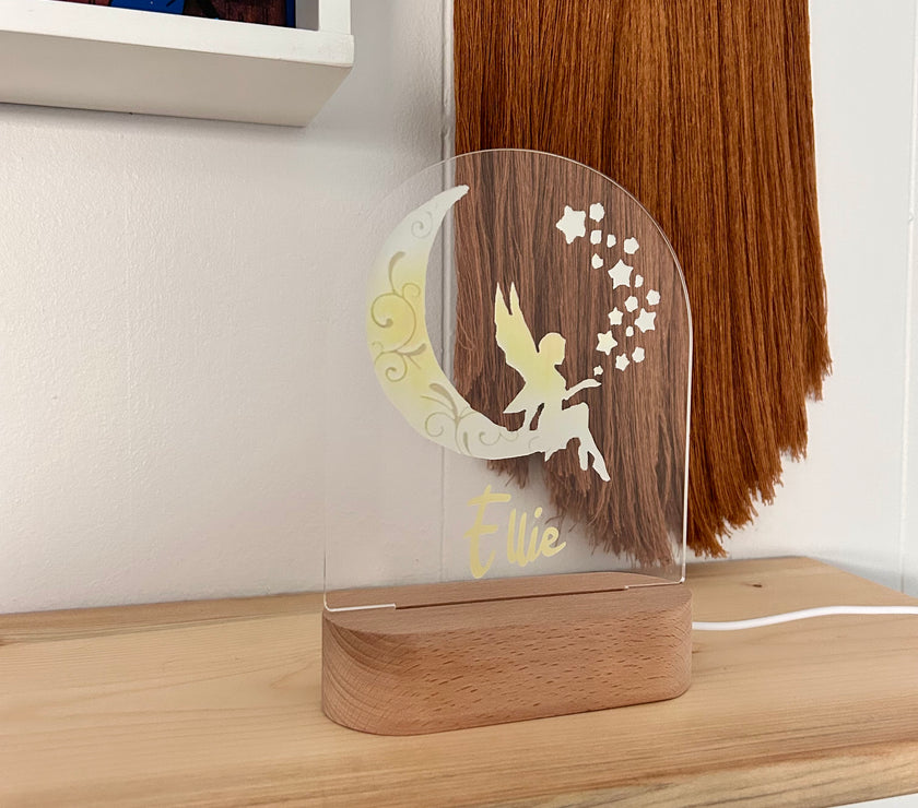 Clear acrylic plaque with fairy design and wooden base on a shelf