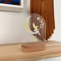 Clear acrylic plaque with fairy design and wooden base on a shelf